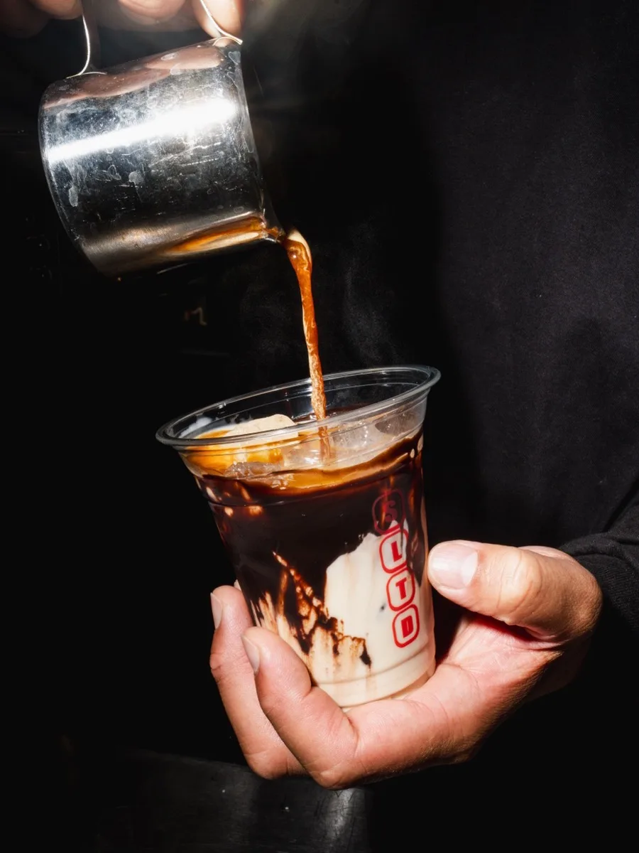 Un expresso versé sur glace dans un gobelet SLTD, tenu en main.