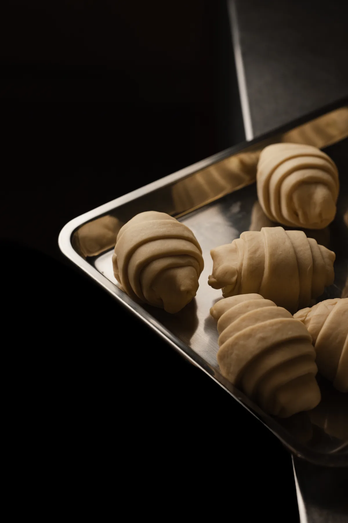 Des salted breads crus, feuilletage roulé apparent, sur un plateau inox avant cuisson.